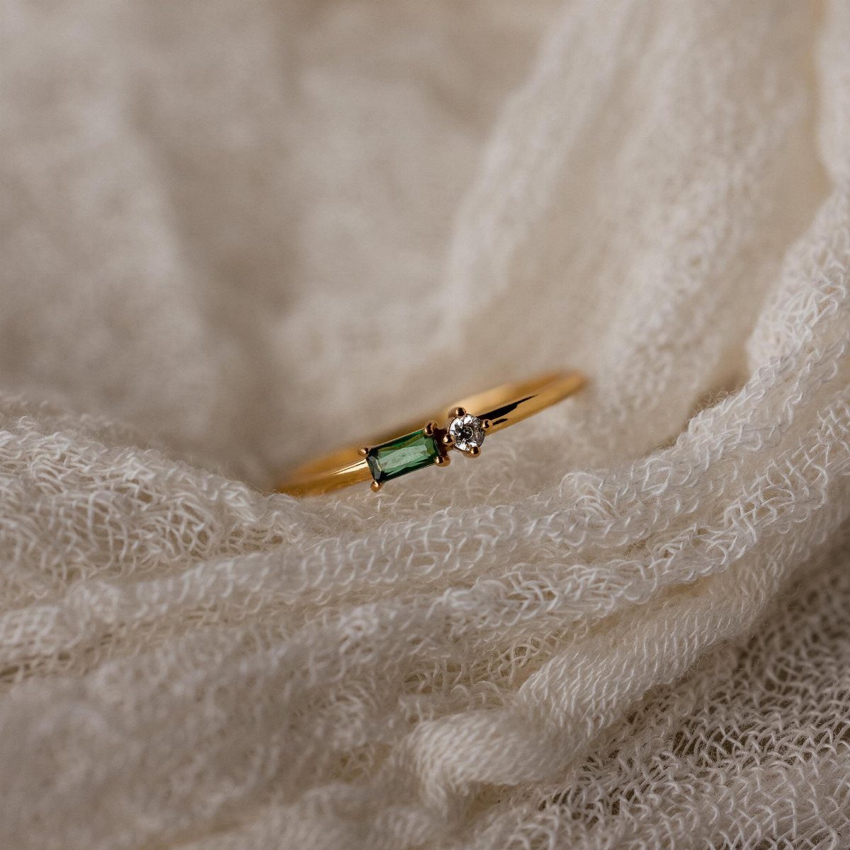 Gold ring with a green gemstone and diamond on white textured fabric