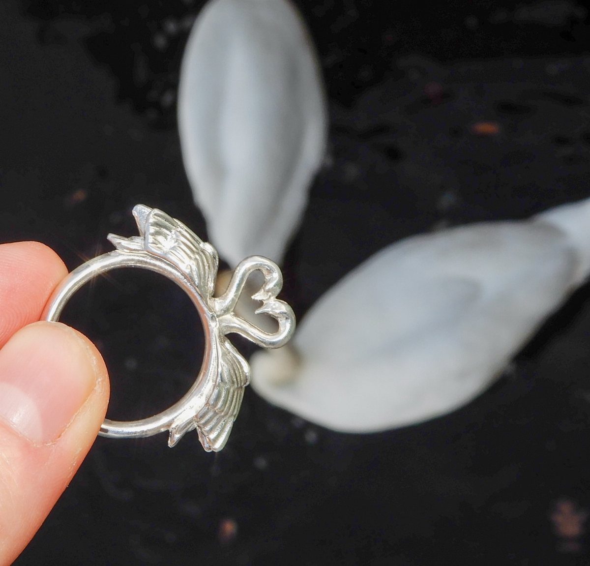 Silver ring with bow and wing details held by a person's fingers.