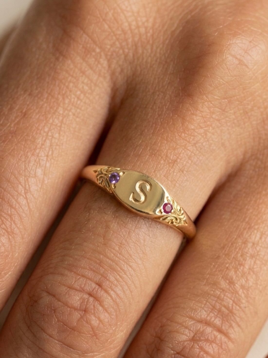 Gold signet ring with engraved letter S and small colorful gemstones on finger