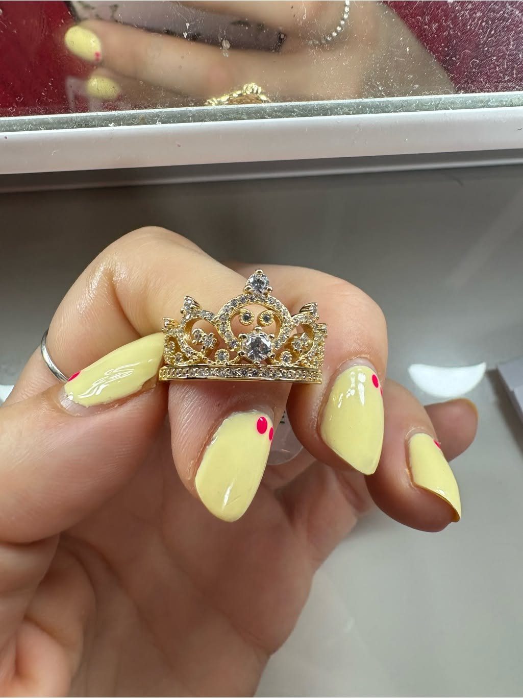 Gold crown ring with crystals held by a hand with yellow nails.