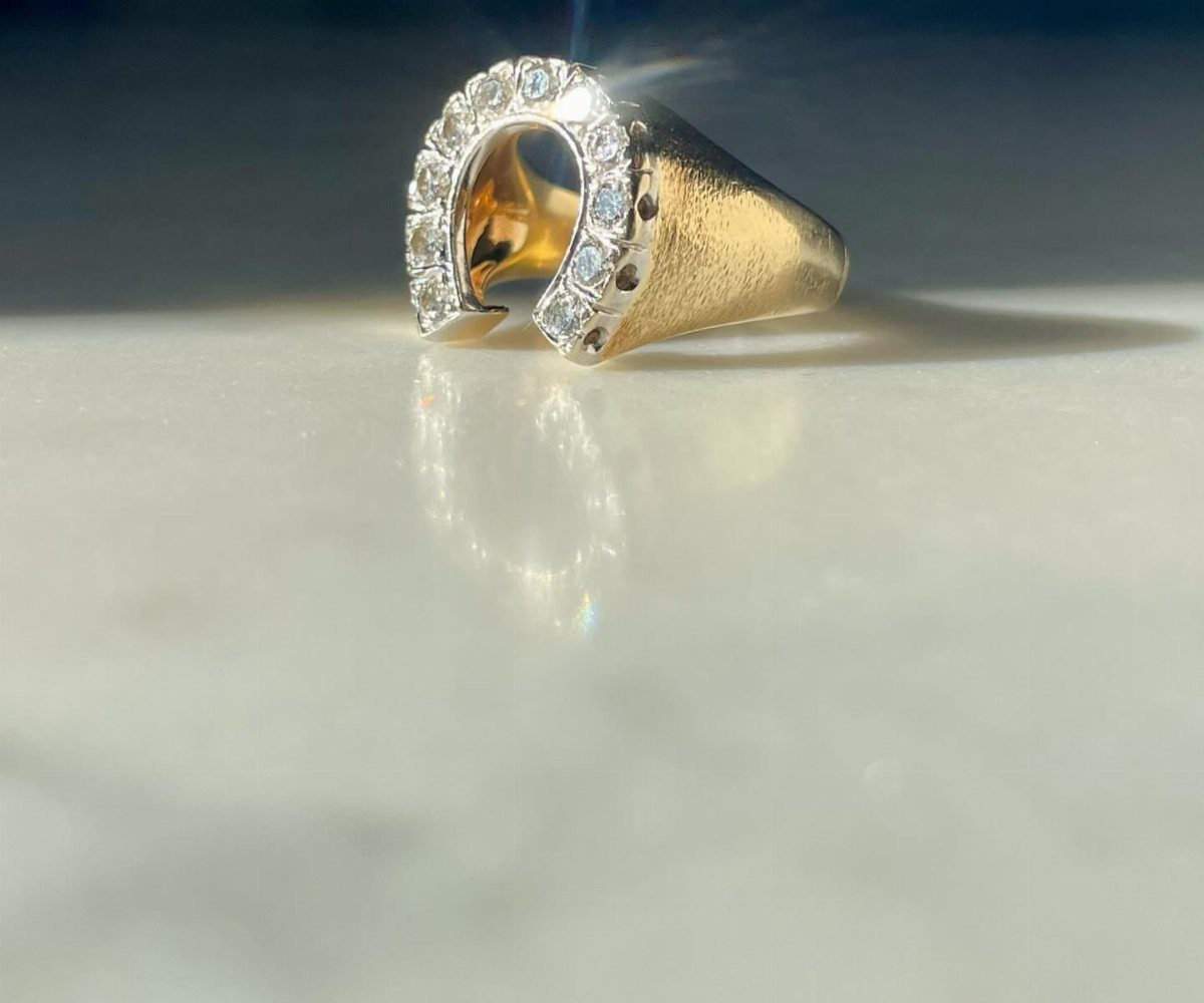 Gold horseshoe ring with small diamonds resting on a white marble surface