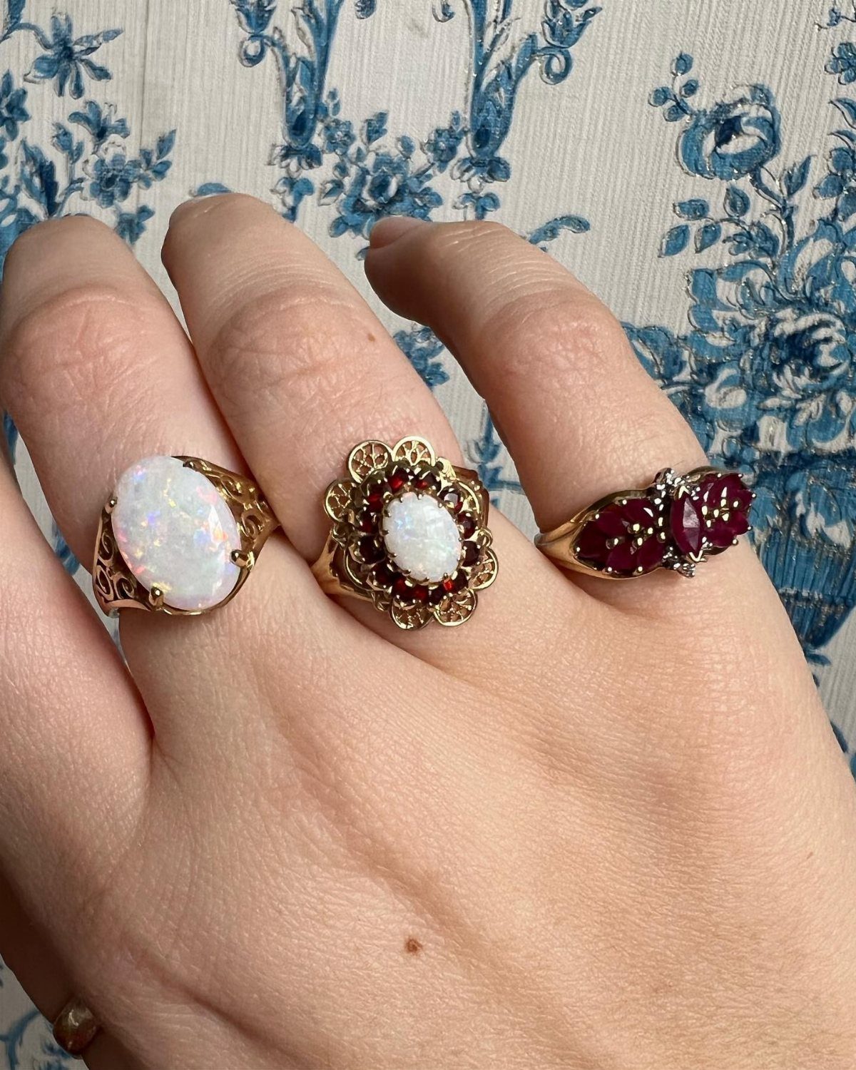 Three ornate gold rings with opals and red gemstones on a hand.