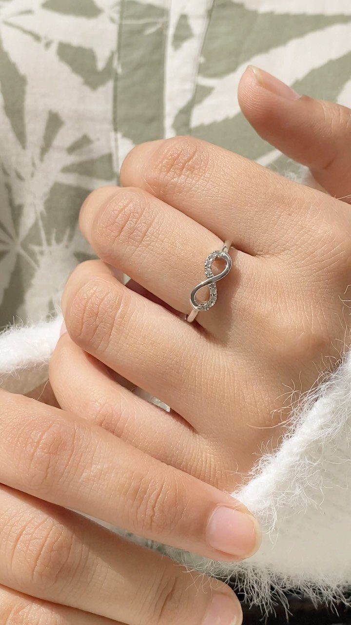 Silver infinity symbol ring with small diamonds worn on a finger.
