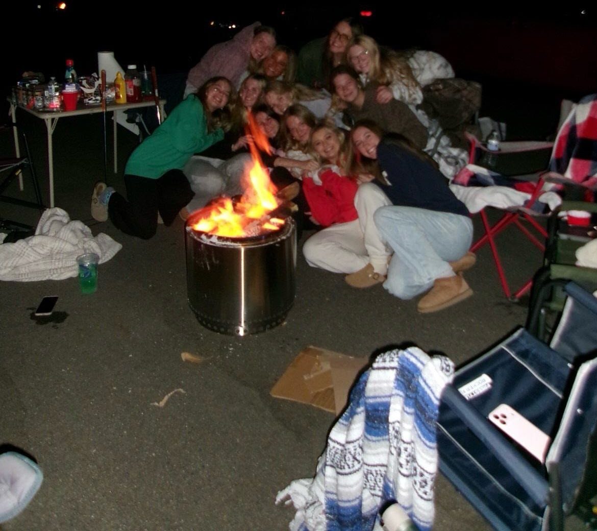 Teenagers gathered around a metal fire pit with a bright flame at night.