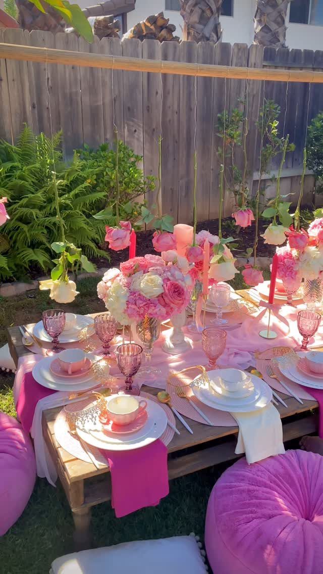 Pink themed party table setting with roses and poufs in a backyard