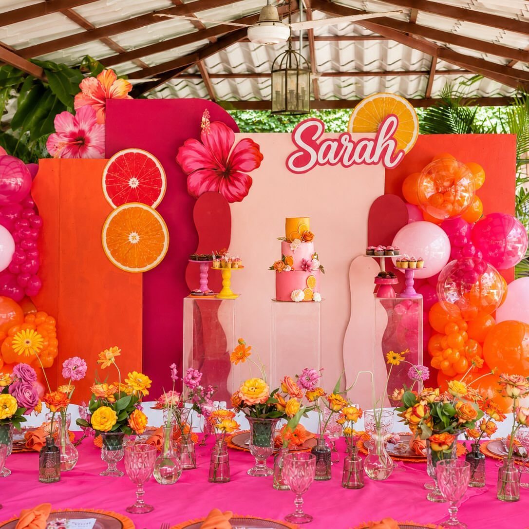 Vibrant pink and orange party decorations with a cake and floral table setting.