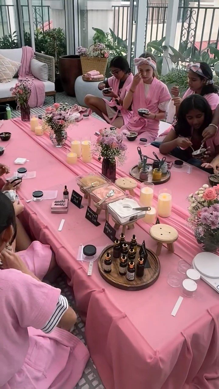 Girls in pink robes at a spa station table with beauty products and flowers.