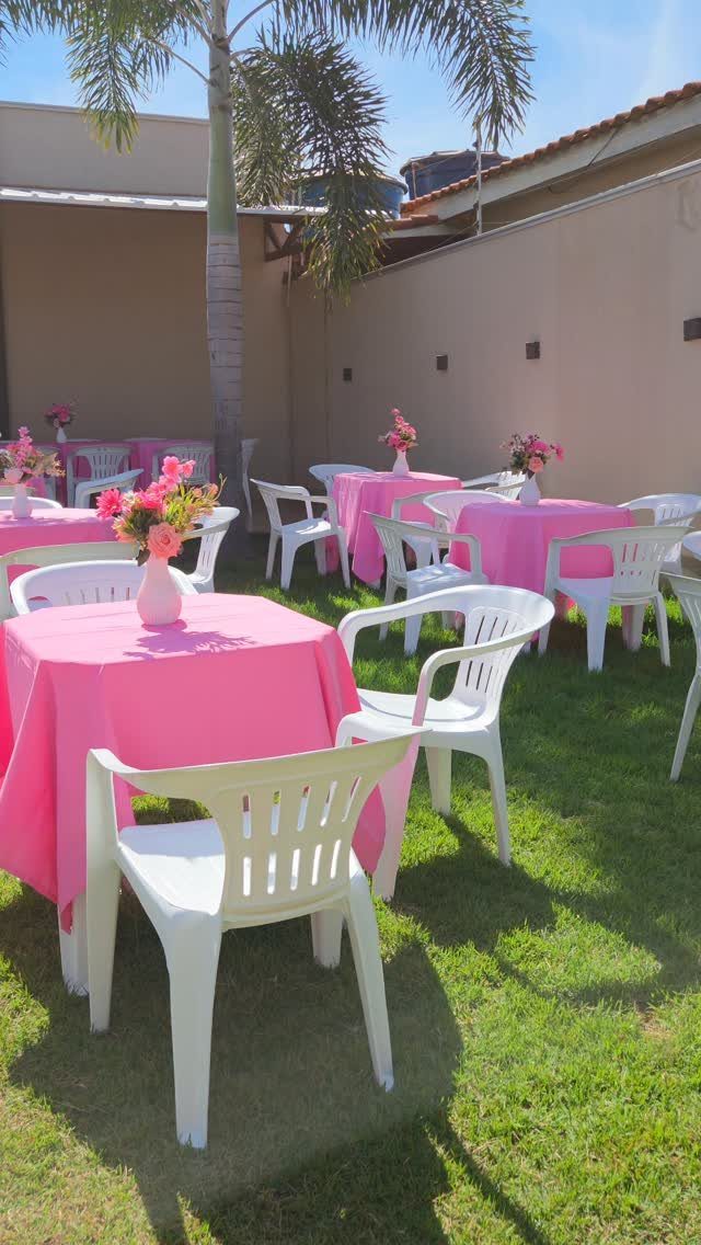 Pink tablecloths and white chairs set up for a party on a lawn