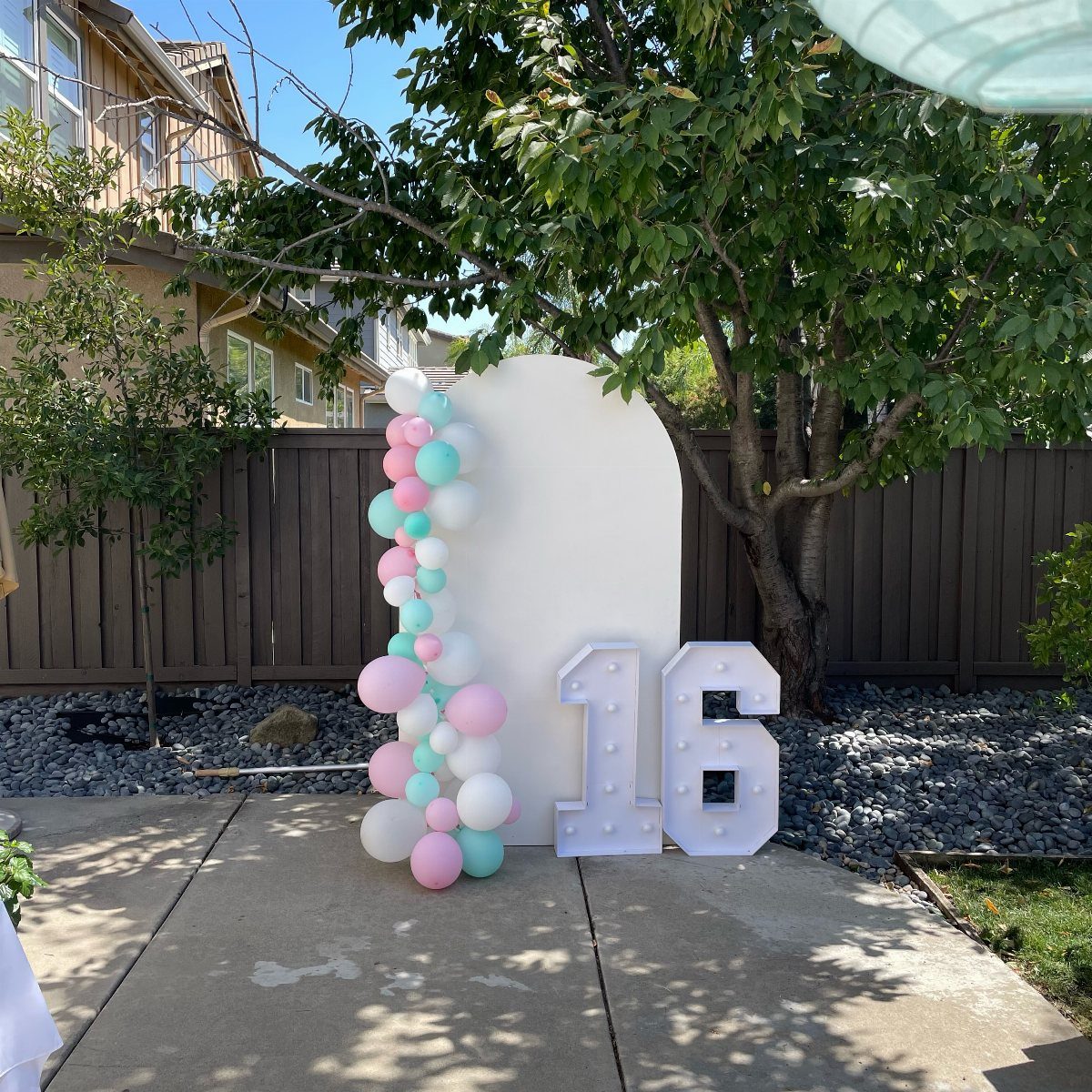 White arched backdrop with pink and mint balloons and illuminated number 16.