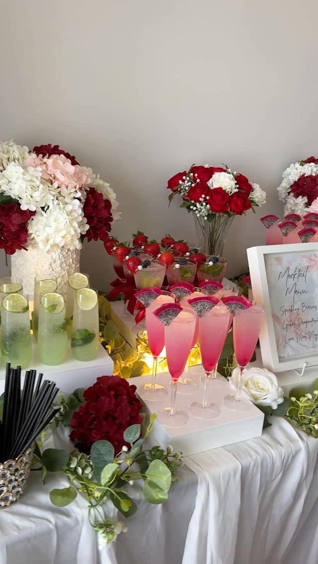 Pink and green drinks in champagne flutes on a table with red flowers.