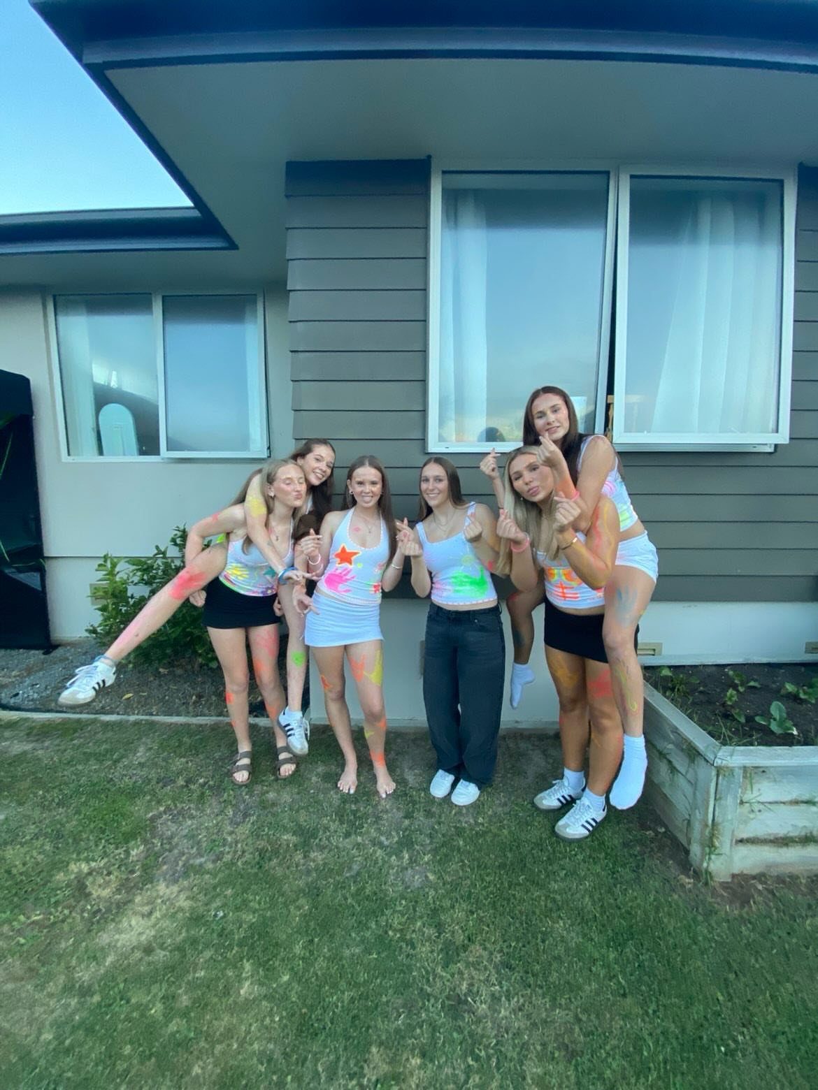 Six teenage girls with neon paint on their clothes posing in a backyard.