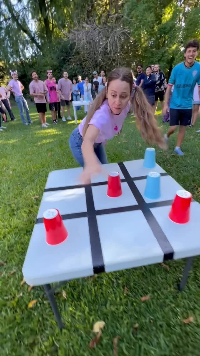 Young woman playing giant tic-tac-toe with plastic cups in a grassy backyard.