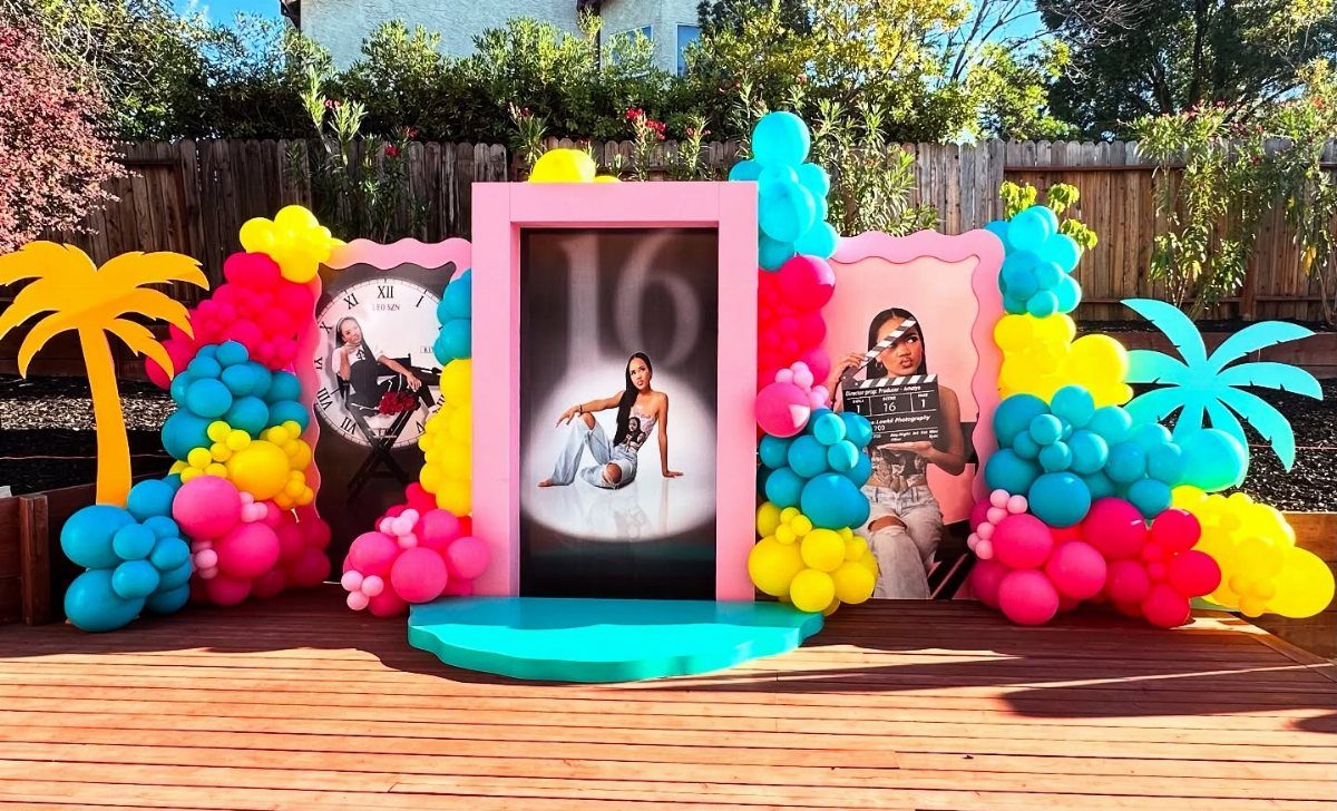 Colorful party backdrop with balloons, palm trees, and photos for a sweet 16.