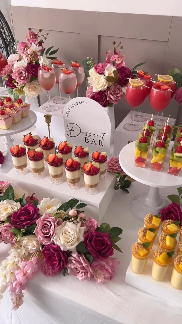 Dessert bar table with strawberry and mango cups, pink drinks, and floral arrangements.