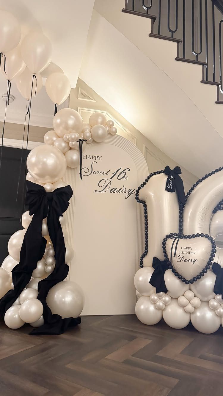 White balloon arch and backdrop with black bows for a Sweet 16 party.