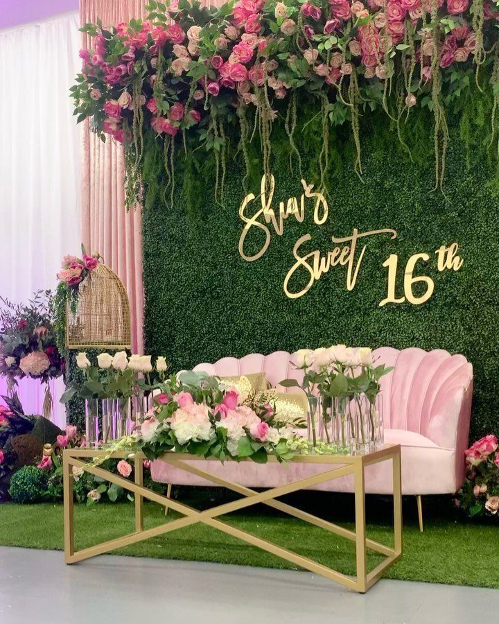 Pink velvet sofa and gold table before a floral hedge wall for Sweet 16.