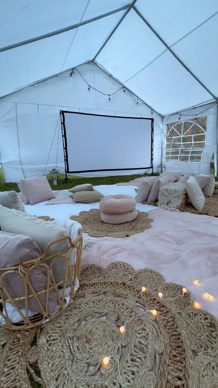 Large projector screen in a white tent with cozy pillows and blankets.