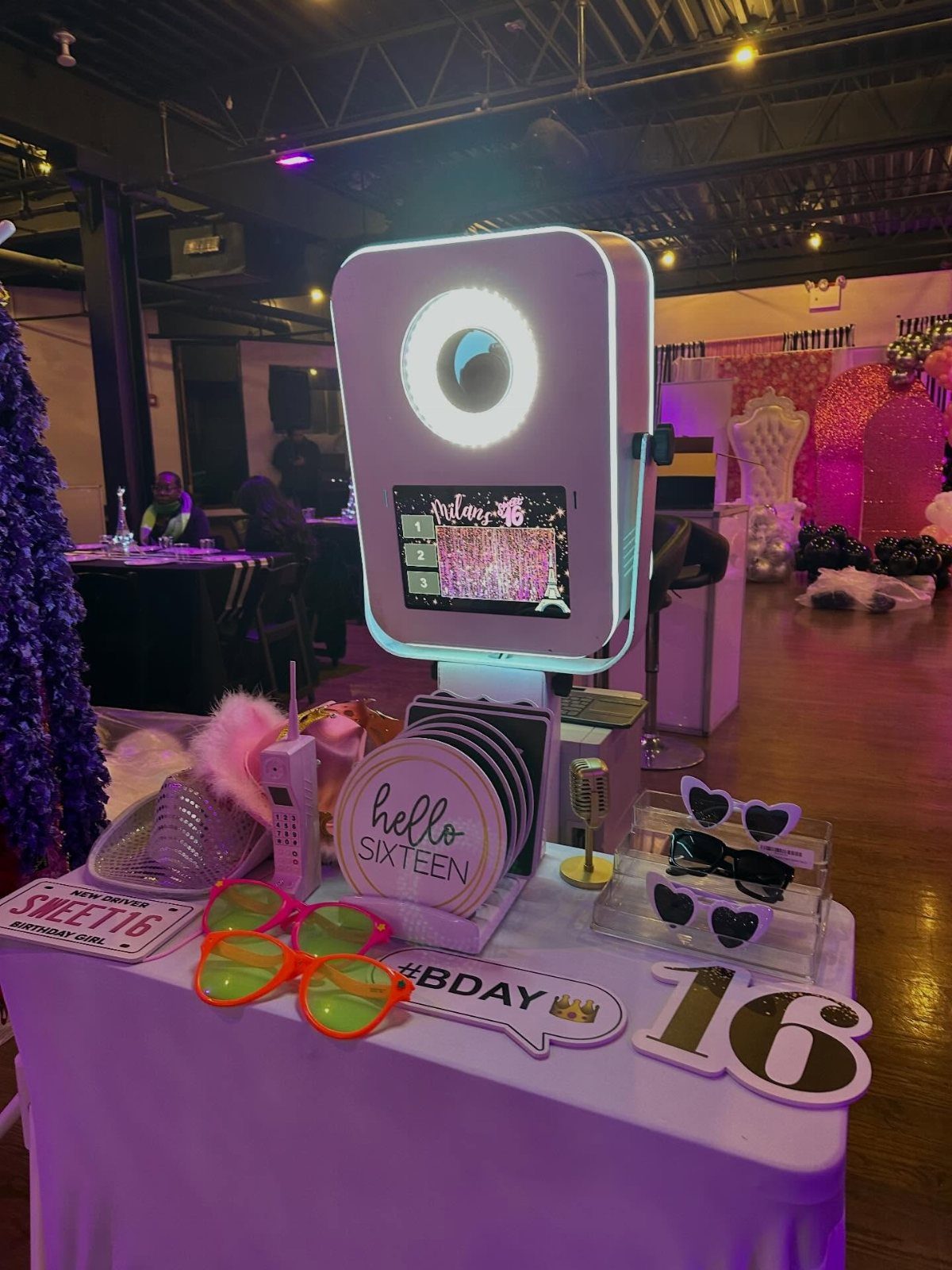 Digital photo booth on a table with heart sunglasses and sweet 16 signs.