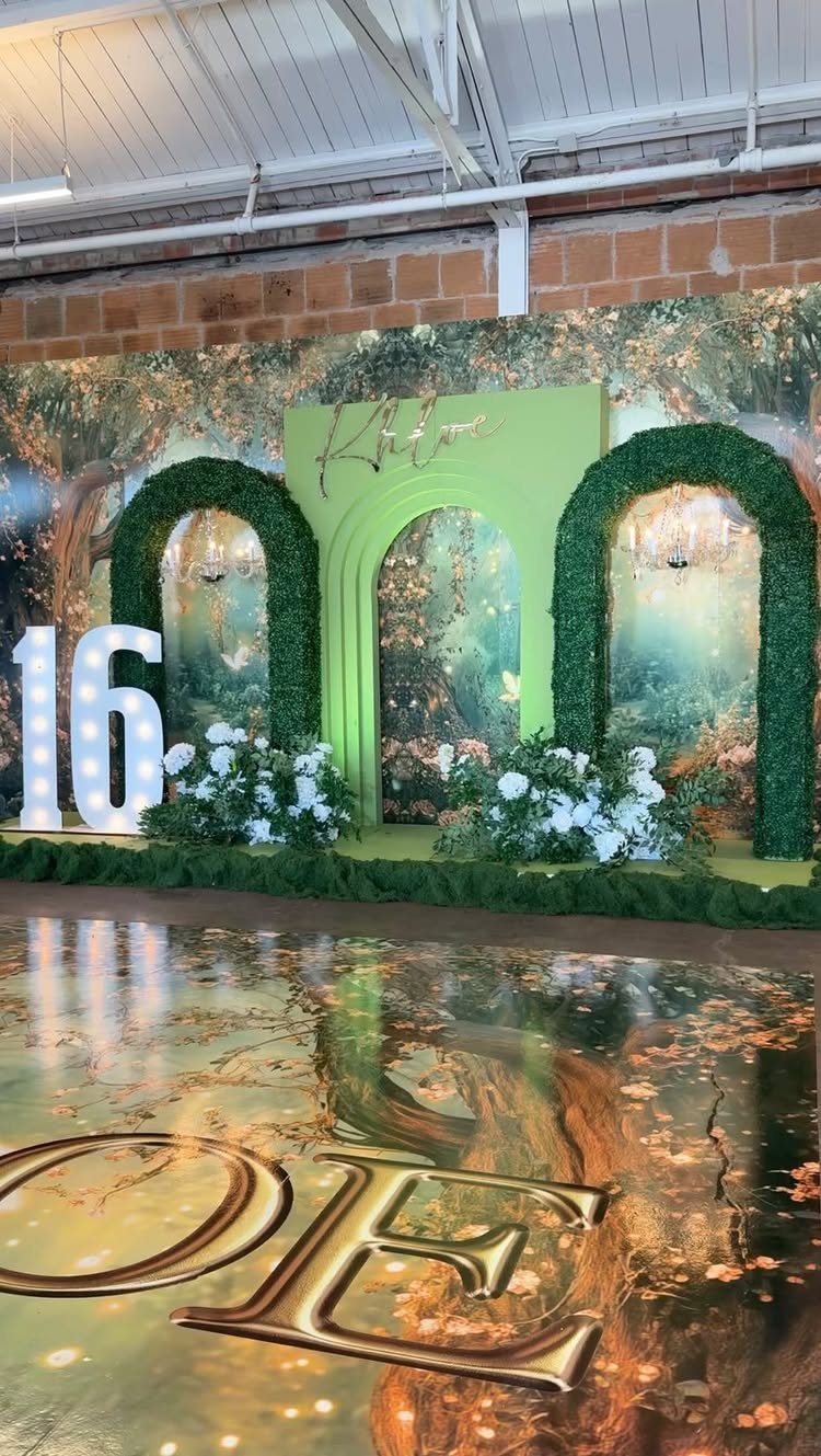 Forest themed party backdrop with green hedge arches, white flowers, and glowing 16 sign.