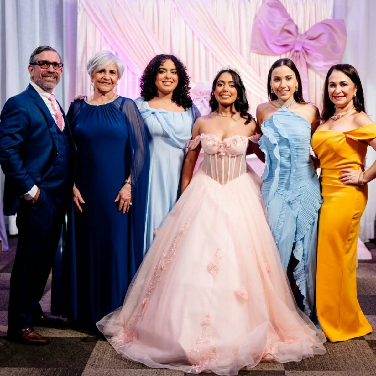 Group of people in formal attire posing around a girl in a pink gown.