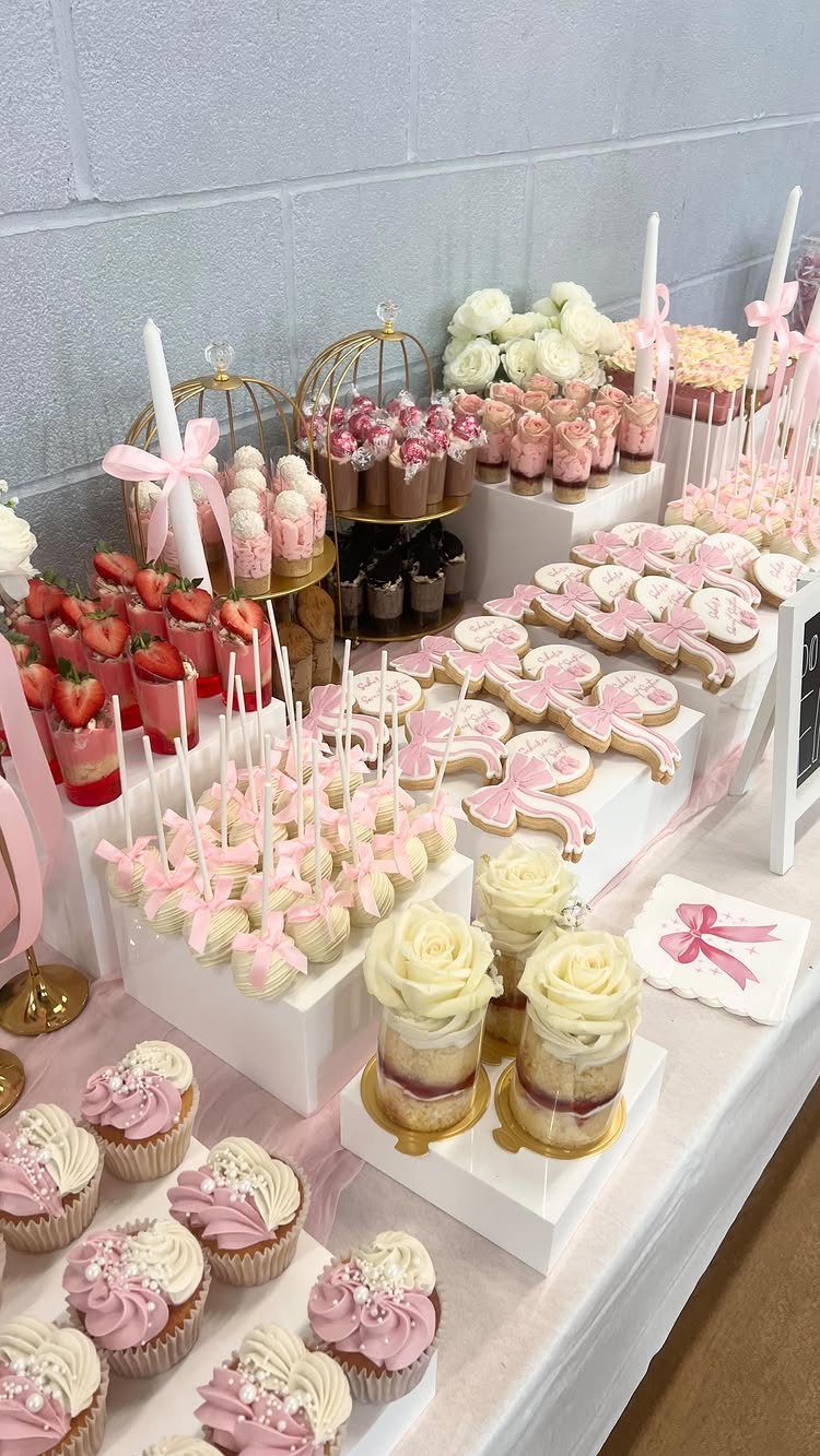Dessert table with pink and white cupcakes, cake pops, and cookies for a party.