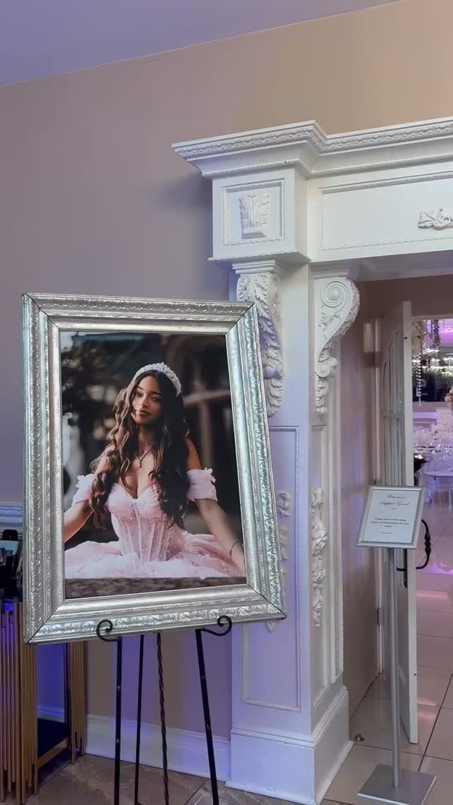 Silver-framed portrait of a girl in a pink dress on a black easel.