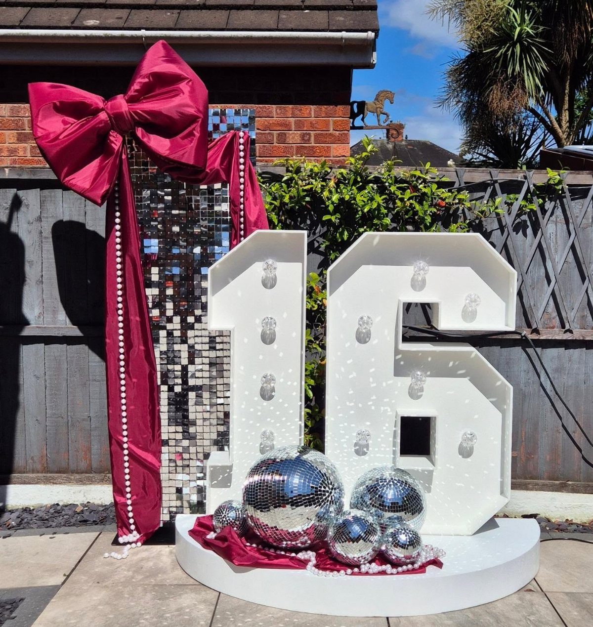 Large white illuminated number 16 with disco balls and a red bow backdrop.