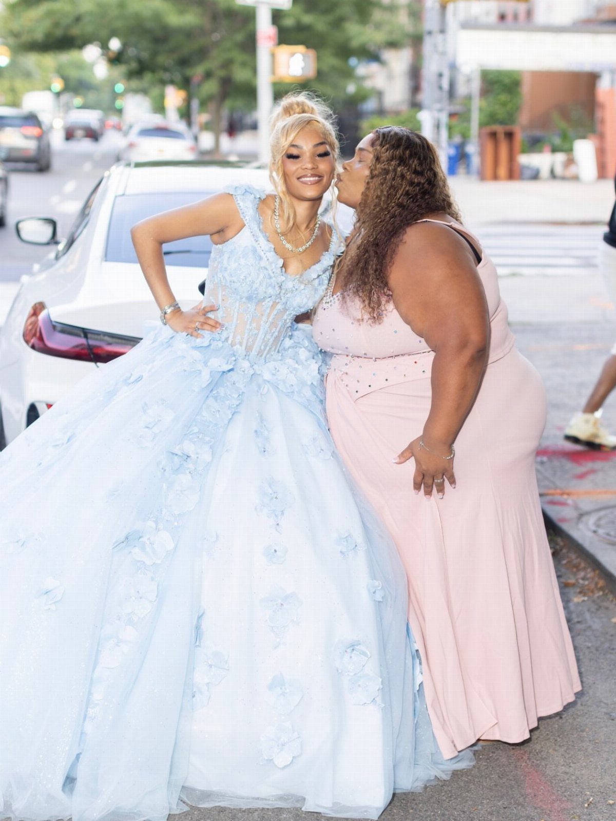 Woman in light blue floral ballgown and woman in pink dress posing outdoors.