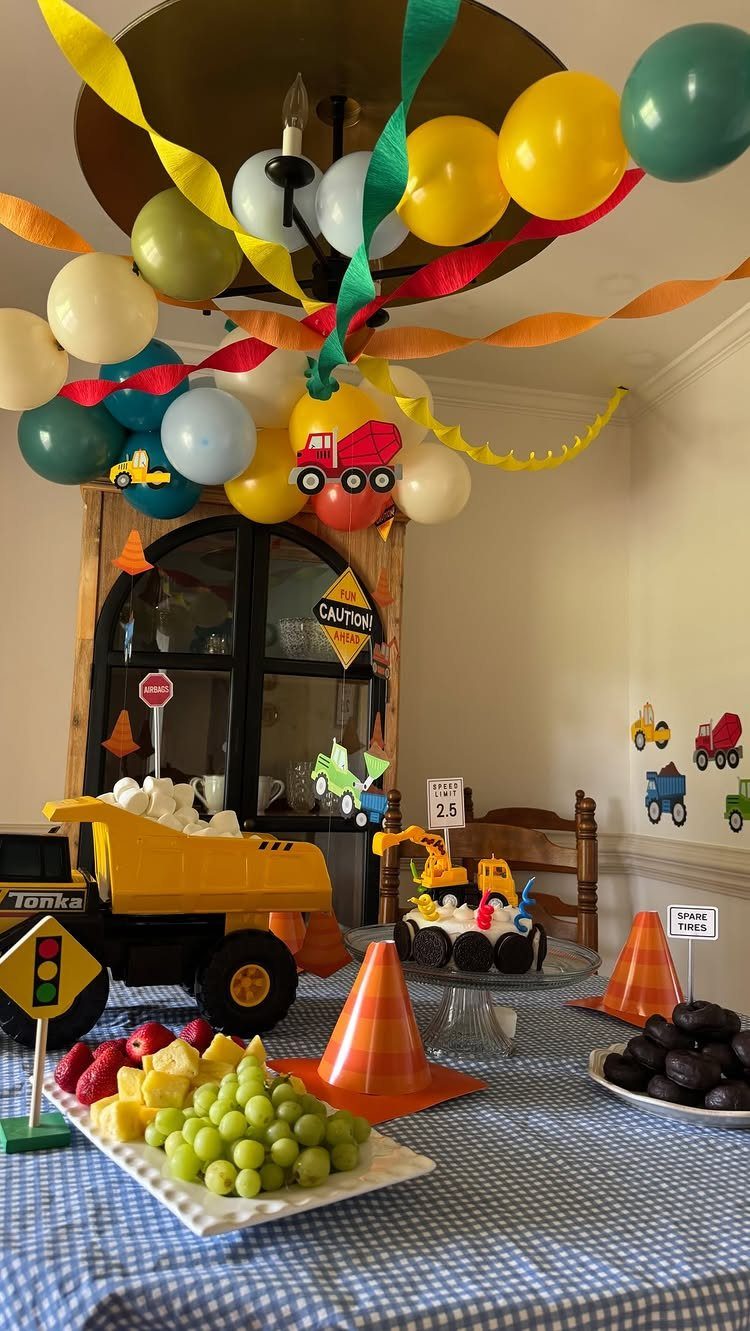 Construction themed birthday party table with balloons, toy trucks, and a decorated cake.