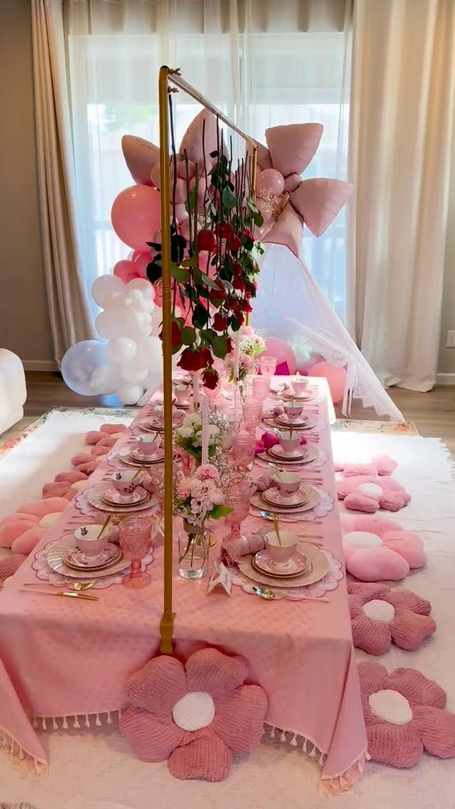 Pink party table setting with balloons, red roses, and flower-shaped floor cushions.