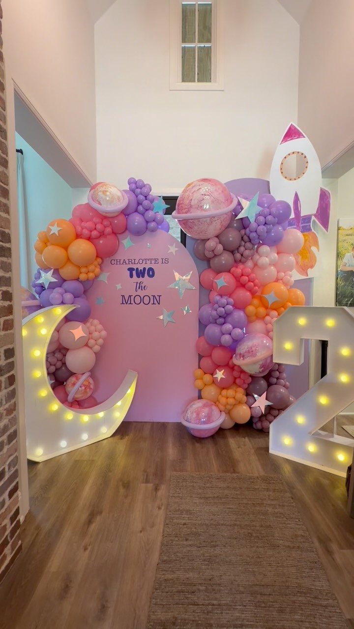Space-themed birthday party setup with pink backdrop, balloons, glowing moon, and rocket ship.