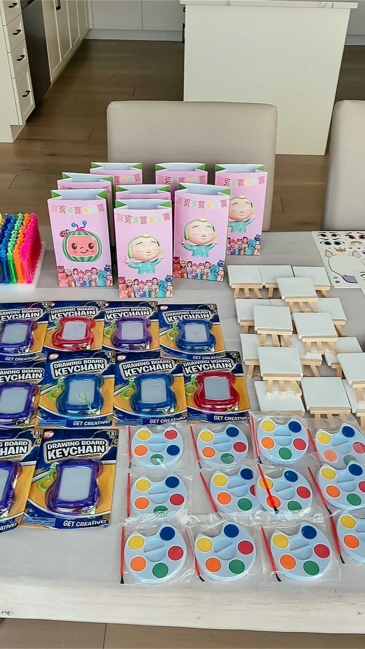 Party favors including pink gift bags, drawing keychains, and paint palettes on a table.