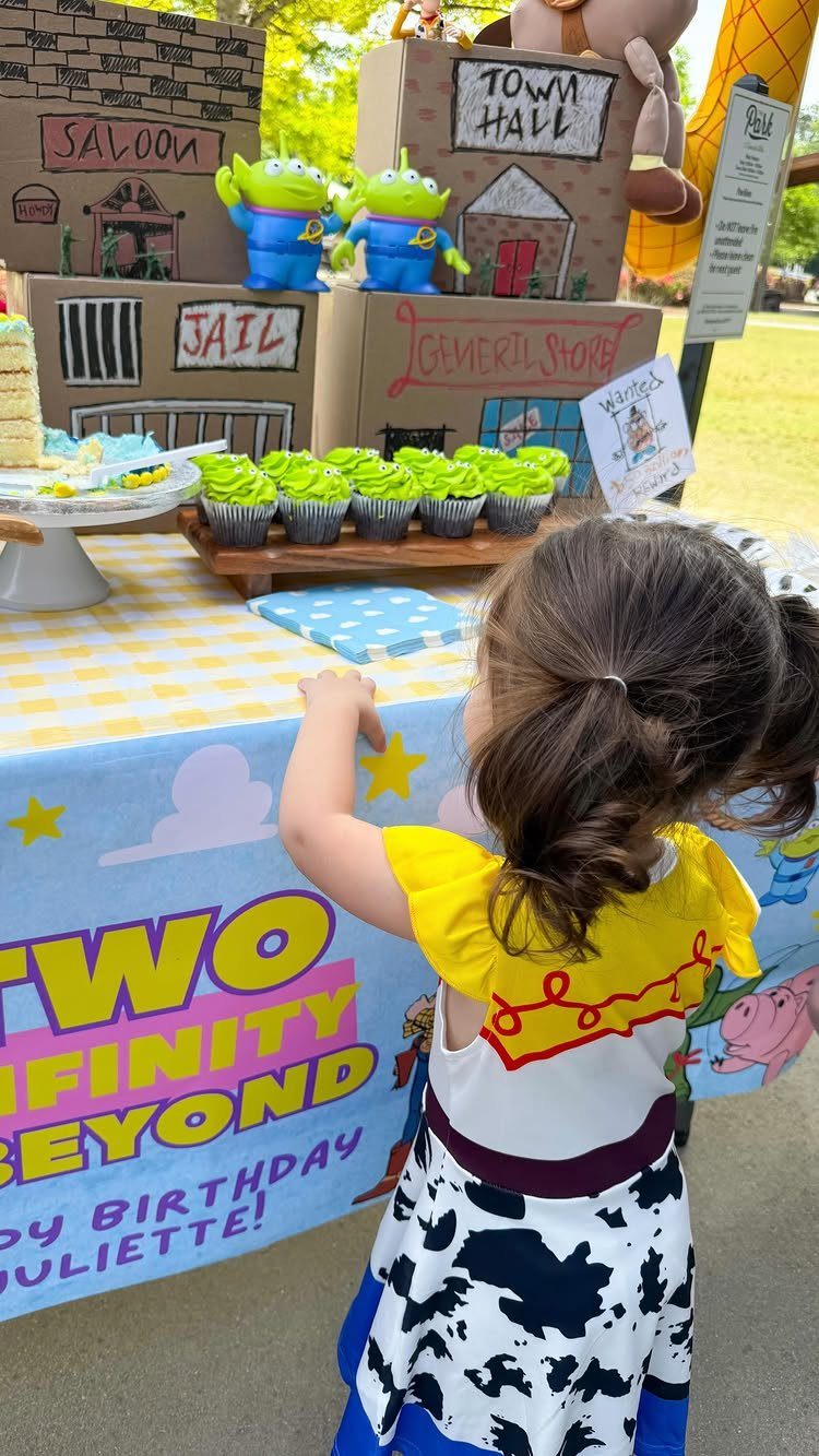 Young girl in cowgirl attire at a Toy Story themed second birthday party table.