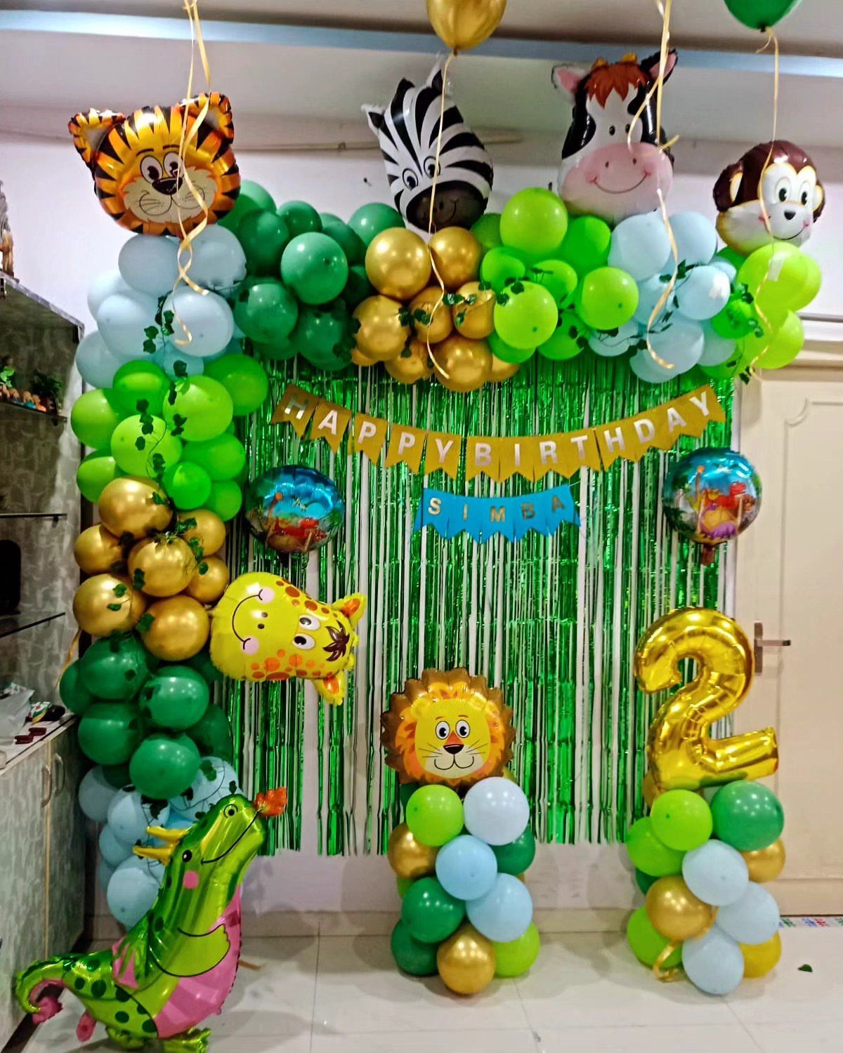 Safari themed birthday decorations with animal balloons, green tinsel, and a gold number 2.