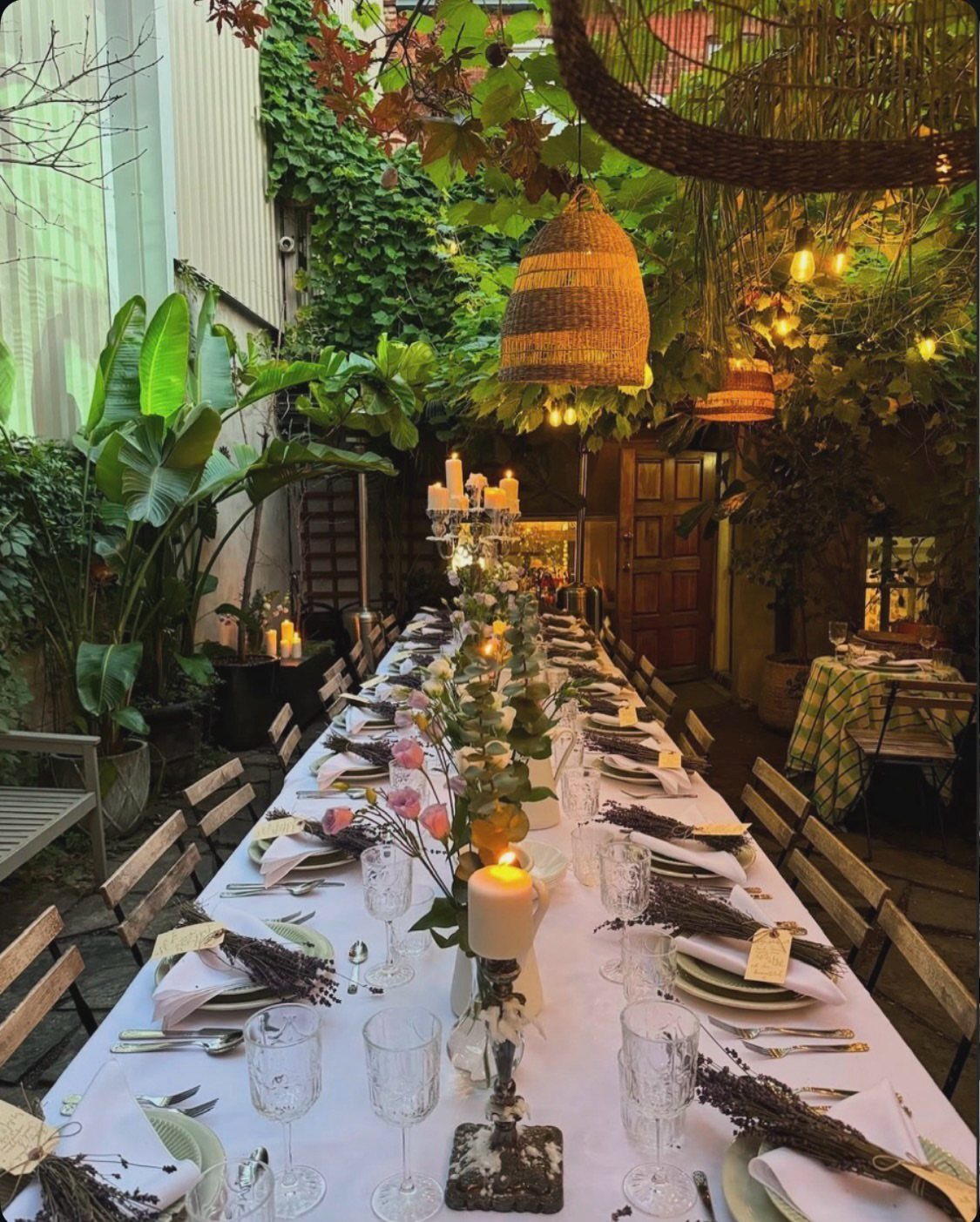 Long outdoor dining table with white linens and floral centerpieces in a lush garden