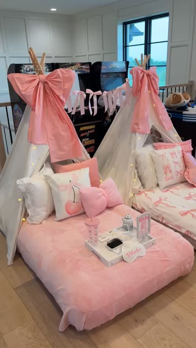 Two white teepee tents with pink bows and plush bedding for a party.