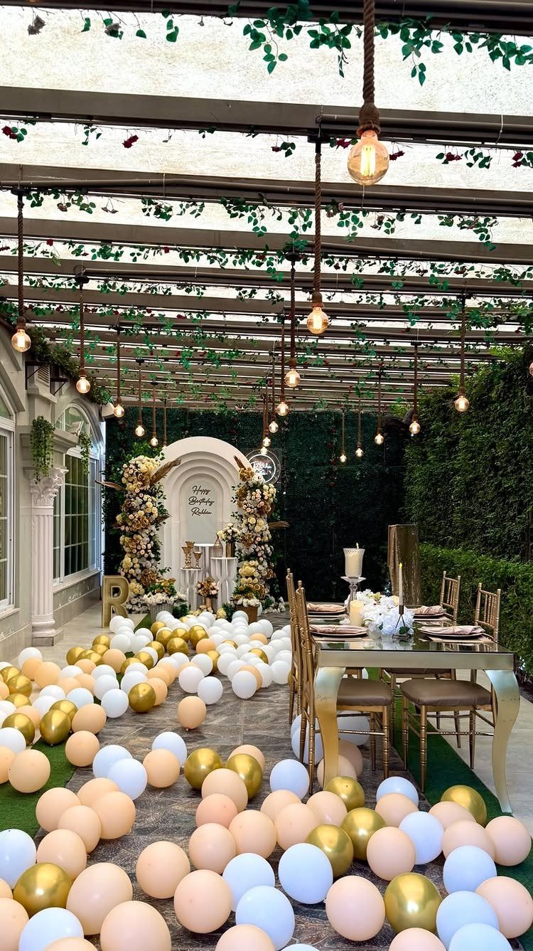 Outdoor party venue with balloons on the floor, a decorated table, and hanging lights.