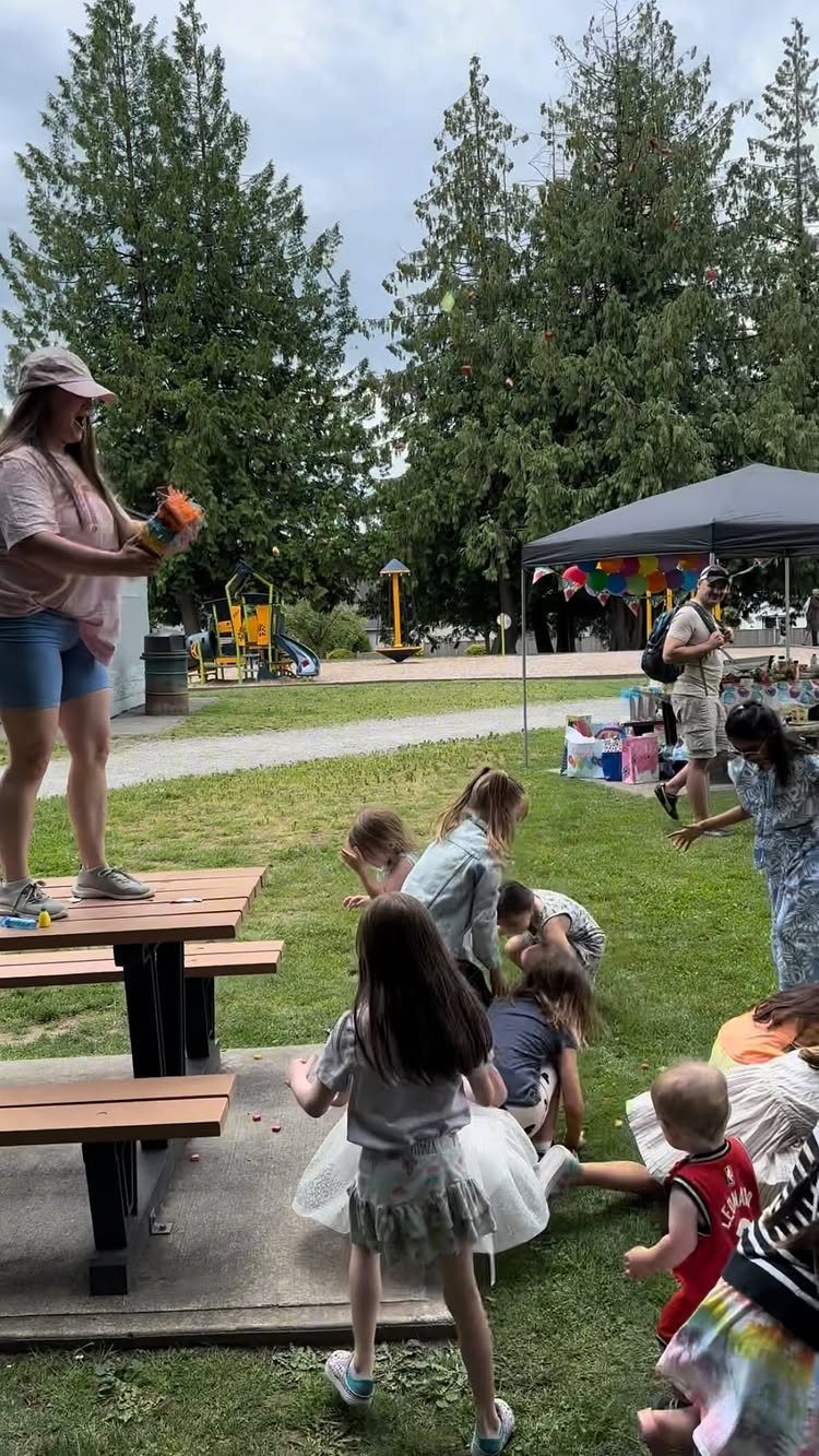 Children and adults gathering on a grassy lawn near a playground and canopy tent.