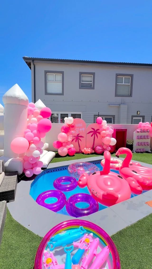 Outdoor swimming pool decorated with pink balloons and flamingo floats for a party.