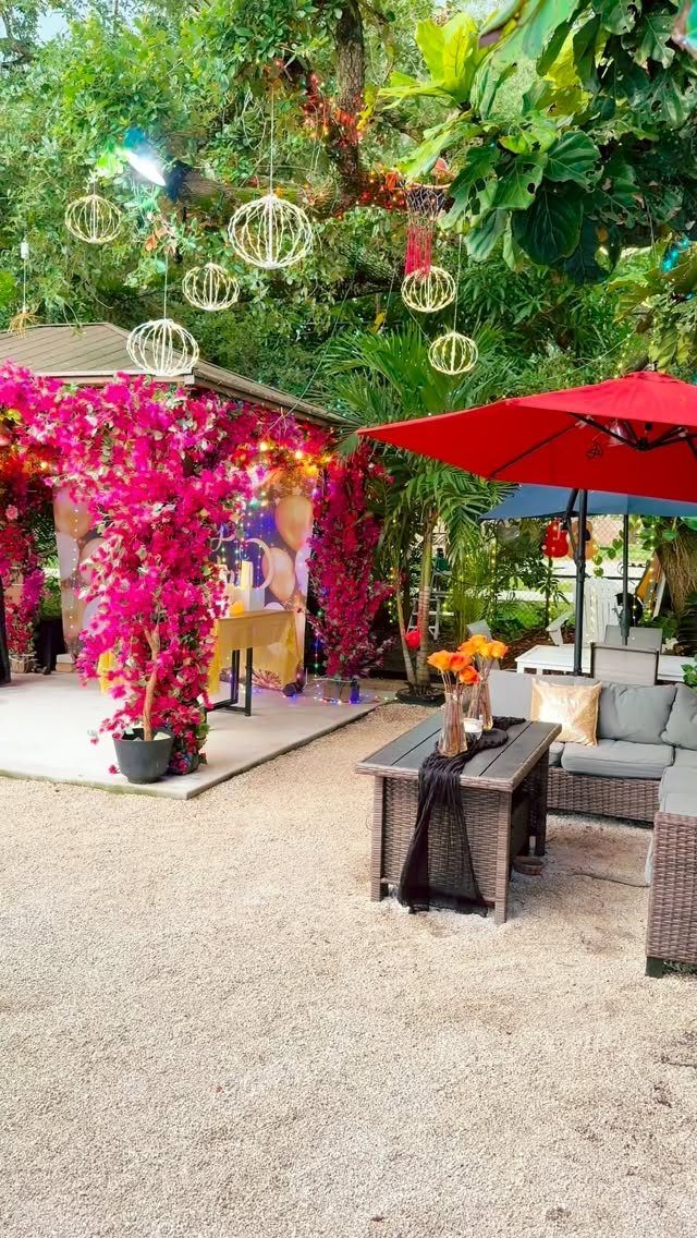 Outdoor garden party setup with pink floral decor, wicker furniture, and red umbrella.